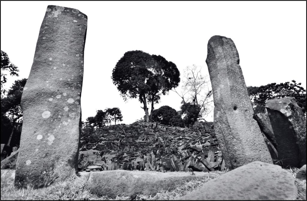 A grayscale photo looking up the terraced slope of Gunung Padang in Indonesia, with the view framed by two large, ancient standing stones of columnar basalt.